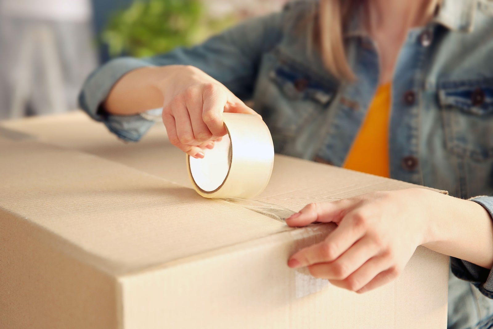 A person sealing a cardboard box with packing tape.